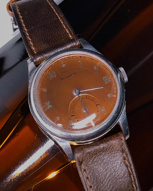 Close view of a Movado watch with a warm patinated dial, small seconds and brown leather strap.
