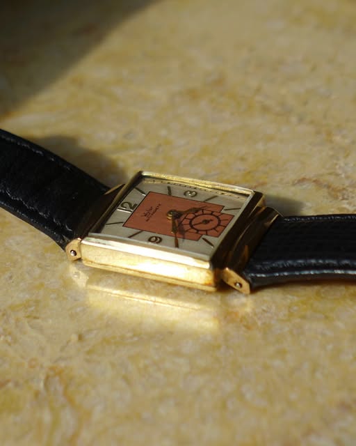 Gold-tone rectangular watch with a coral and black graphic dial, resting on pale stone.